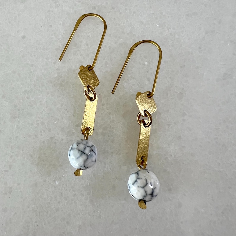 K&ouml;nnte beinhalten: Goldene Ohrh&auml;nger mit wei&szlig;en marmorartigen Perlen und goldenen geometrischen Formen.