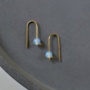 Könnte beinhalten: Ein Paar goldene Creolen mit einem hellblauen Opal-Edelstein an jedem Creolen.
