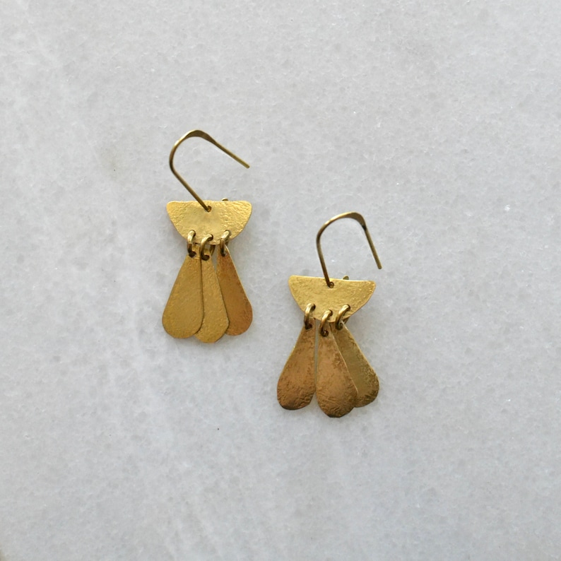 May include: A pair of gold-toned dangle earrings with a geometric design. Each earring features a small, curved top piece with three teardrop-shaped pendants hanging below.