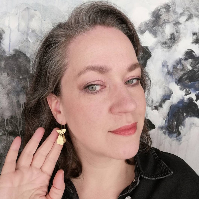 May include: A woman with gray hair wearing gold geometric earrings. The earrings are made of multiple small, flat, triangular shapes.
