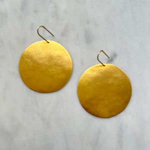Peut inclure: Une paire de boucles d'oreilles rondes en forme de disque de couleur or avec une texture martelée.