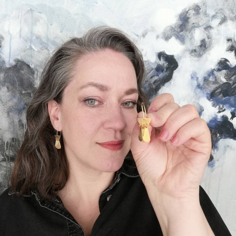 May include: A pair of gold-toned earrings with a geometric design. The earrings are made of multiple small, overlapping pieces of metal.