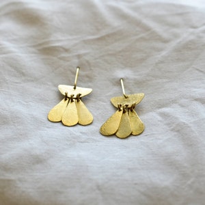 May include: A pair of gold earrings with a geometric design. Each earring features a small, curved top piece with three teardrop-shaped pieces hanging below.