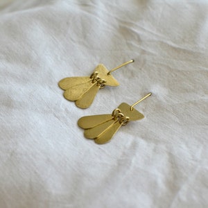 May include: A pair of gold-toned earrings with a fan-shaped design. Each earring features three overlapping teardrop-shaped pieces connected by a small chain.