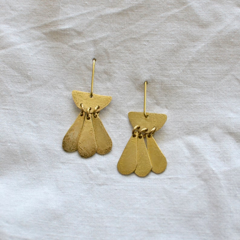 May include: A pair of gold-toned dangle earrings with a teardrop shape and a curved top. The earrings have a hammered texture.