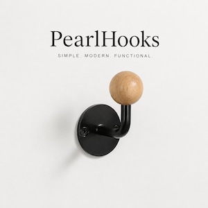 Puede incluir: Un gancho de pared de metal negro con un pomo redondo de madera. El gancho está montado sobre una base circular. El texto "PearlHooks" y "SIMPLE. MODERN. FUNCTIONAL." están encima del gancho.