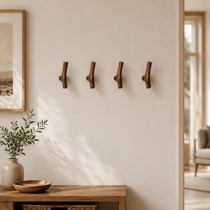May include: Four dark brown wooden wall hooks mounted in a horizontal row. Each hook features a Y-shaped design with a central base and two upward-curving arms, providing a functional solution for hanging items on a flat, neutral-coloured wall surface.