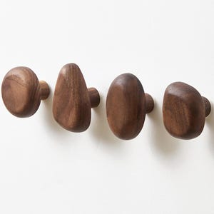 Könnte beinhalten: Vier Holzschrankknöpfe in verschiedenen organischen Formen. Jeder Knopf hat eine satte, dunkelbraune Farbe und scheint aus massivem Holz zu bestehen. Die Knöpfe sind auf einer weißen Oberfläche montiert und zeigen ihre natürliche Maserung und einzigartigen Formen.