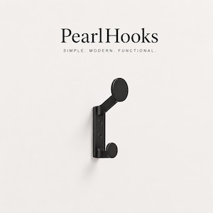 Könnte beinhalten: Ein mattschwarzer Wandhaken mit zwei runden Haken und einer rechteckigen Basis, die mit zwei sichtbaren Schrauben befestigt ist. Der Text PearlHooks SIMPLE. MODERN. FUNCTIONAL. steht in schwarzer Schrift über dem Haken.