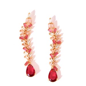Könnte beinhalten: Ein Paar goldfarbene Ohrringe mit Kaskadendesign. Jeder Ohrring hat eine Reihe rechteckiger, rosa und klarer Kristalle, die in einem tropfenförmigen, rubinroten Stein enden. Die Ohrringe sind vor einem weißen Hintergrund platziert.