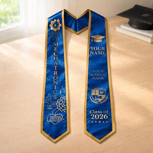 May include: A blue graduation sash with gold trim and text. One side reads "MECHATRONICS" with circuit board graphics. The other side has space for "YOUR NAME" and "YOUR SCHOOL NAME", plus "Class of 2026". A mortarboard is in the background.