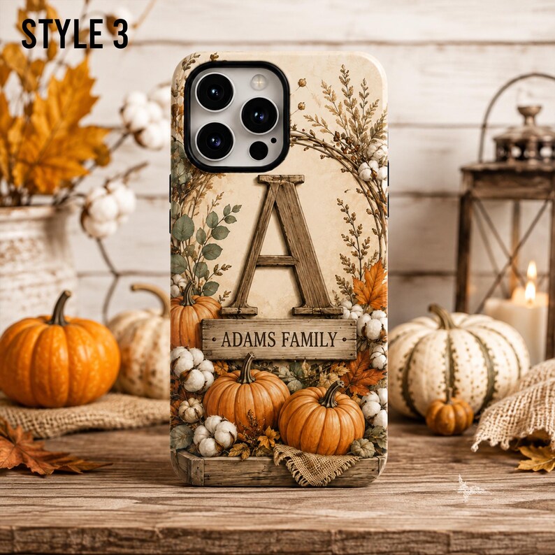 May include: A phone case featuring a large wooden letter A above a rectangular sign with the text ADAMS FAMILY. The design includes orange pumpkins, white gourds, autumn leaves, and dried foliage on a cream background with a camera cutout.