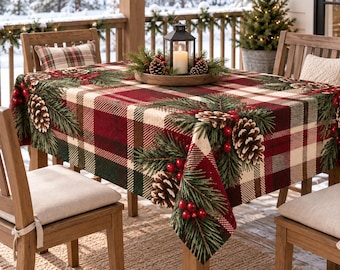 May include: A rectangular tablecloth featuring a red, green, and cream plaid pattern decorated with printed illustrations of pine branches, brown pinecones, and clusters of bright red berries, draped over a wooden table with a lantern centerpiece.