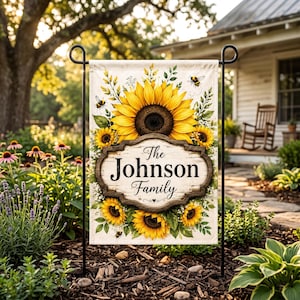 May include: A personalized garden flag featuring a sunflower design with the text "The Johnson Family". The flag has a wooden-style frame and is decorated with yellow sunflowers and bees. The flag is displayed in a garden setting.