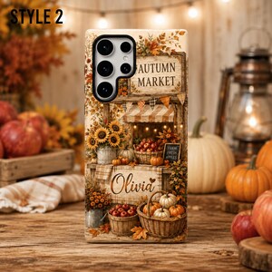 May include: A phone case featuring an autumn market scene with sunflowers, pumpkins, and baskets of apples. The design includes the text "AUTUMN MARKET", "FARM FRESH APPLES", and the name "Olivia" in script font, set against a rustic fall backdrop.