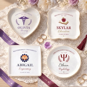May include: Four white ceramic trinket dishes with gold rims, each personalized with a university name, student's name, and graduation year. The shapes include a heart, square, and circle, with a medical symbol, apple, gear, and psychology symbol.