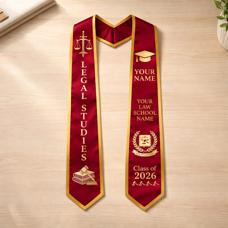 May include: A maroon graduation sash with gold trim and text. The left side reads "LEGAL STUDIES" with a gavel and books icon. The right side has space for "YOUR NAME" and "YOUR LAW SCHOOL NAME", with "Class of 2026" at the bottom.