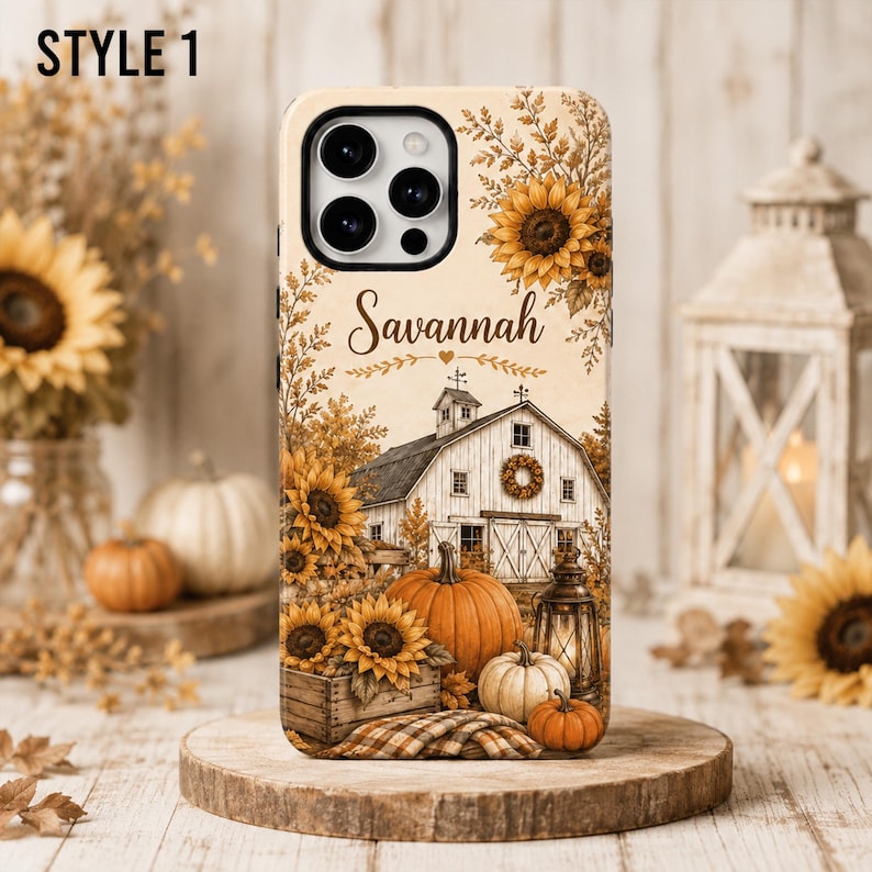 May include: A phone case featuring a rustic farm scene with a white barn, sunflowers, pumpkins, and a lantern. The name Savannah is printed in a script font above the barn. The design includes autumn foliage and a plaid fabric texture at the base.