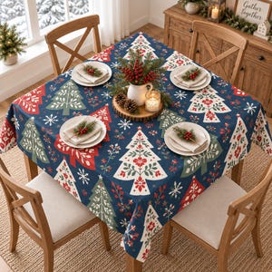 May include: A square navy blue tablecloth featuring a repeating pattern of stylized Christmas trees in red, white, and green, accented with white snowflakes and small floral motifs. The table is set with four white plates, each topped with a folded napkin.