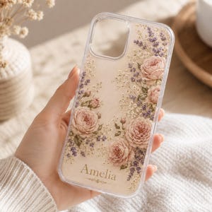 May include: Clear phone case with a floral design featuring pink roses, purple lavender, and small white flowers. The name "Amelia" is printed in a script font at the bottom of the case.