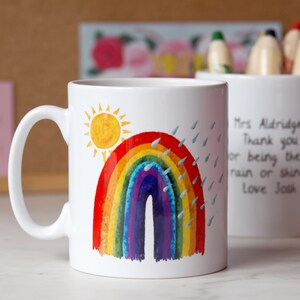 May include: White ceramic mug with a colorful rainbow, sun, and raindrops illustration. The mug has a handwritten message that reads "Mrs Aldridge Thank you for being the best rain or shine love Josh".