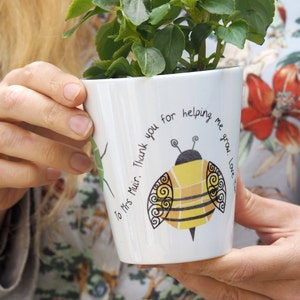 May include: White ceramic planter with a bee illustration and the text "Thank you for helping me grow. Love..."  The planter is decorated with a green leaf design and the text "To Mrs. Muir."