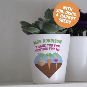 May include: A white ceramic plant pot containing a green succulent. The pot features the text "MRS ROBINSON THANK YOU FOR ROOTING FOR ME" above a heart-shaped illustration of three vegetables. An orange circular sticker reads "WITH SOIL DISCS & CARROT SEEDS".