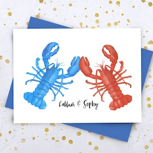 May include: A white card with two lobsters facing each other. The lobster on the left is blue and the lobster on the right is red. The text "Callum & Sophy" is written below the lobsters.