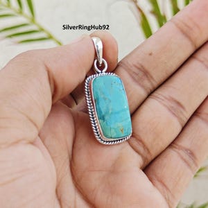 May include: A rectangular turquoise pendant set in a silver frame with a twisted rope border design. The stone is a vibrant blue-green colour with natural brown matrix veining. A silver bail is attached to the top for hanging on a chain.