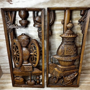 May include: Two rectangular dark brown wooden wall plaques featuring carved relief designs. The left plaque depicts a vintage coffee grinder with wheels, while the right plaque shows a wood-burning stove with a chimney and a small coal bucket.