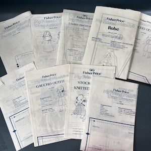 May include: A collection of white paper sewing patterns for Fisher-Price My Friend Mandy dolls, featuring various clothing designs like a robe, sun dress, and gaucho outfit, with printed illustrations, text instructions, and technical diagrams.