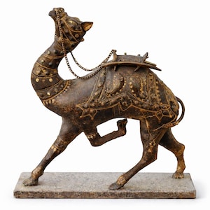 Op de afbeelding: Een bronzen kameelsculptuur met ingewikkelde details. De kameel is versierd met decoratieve zadeldekens en een hoofdstel met een ketting. De sculptuur is gemonteerd op een rechthoekige stenen basis, met een rijke, verouderde patina.