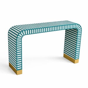 Puede incluir: Una consola moderna con un diseño curvo. La mesa presenta un patrón de rayas turquesas y blancas en la parte superior y los lados. La base de las patas tiene un acabado dorado. La mesa mide aproximadamente 122 cm de largo.