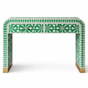 Puede incluir: Una consola con estampado verde y blanco con dos cajones. La mesa tiene un diseño curvo con detalles dorados en las patas. El intrincado patrón presenta elementos geométricos y florales.