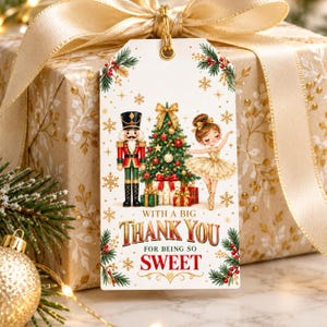 May include: A rectangular white gift tag featuring a nutcracker, a decorated Christmas tree, and a ballerina. The text reads WITH A BIG THANK YOU FOR BEING SO SWEET. The design includes pine branches, red berries, and gold snowflakes.