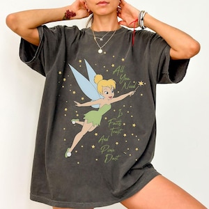 May include: Dark gray t-shirt featuring a graphic of Tinkerbell with the text "All You Need Is Faith Trust And Pixie Dust". The cartoon fairy is wearing a green dress and has blue wings. Gold stars are scattered around the fairy.
