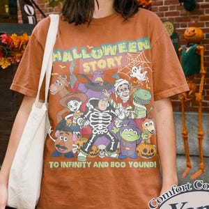 May include: Orange Comfort Colors t-shirt with a Halloween graphic featuring cartoon characters and the text "HALLOWEEN STORY" and "TO INFINITY AND BOO YOUND!". The shirt has a crew neck and short sleeves.