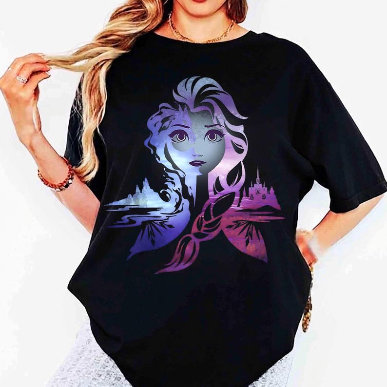 以下が含まれることがあります： 紫と青の色合いの女性の顔のグラフィックが特徴の黒いTシャツ。デザインには城と風景の要素が含まれています。シャツは半袖でカジュアルなスタイルです。