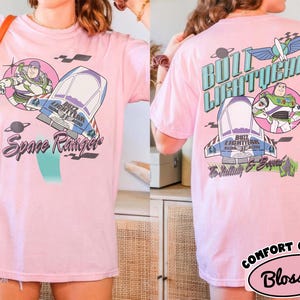May include: A light pink t-shirt featuring Buzz Lightyear graphics on the front and back. The front displays Buzz Lightyear, a spaceship, and the text Space Ranger. The back shows Buzz Lightyear, a spaceship, and the text Buzz Lightyear To Infinity & Beyond.