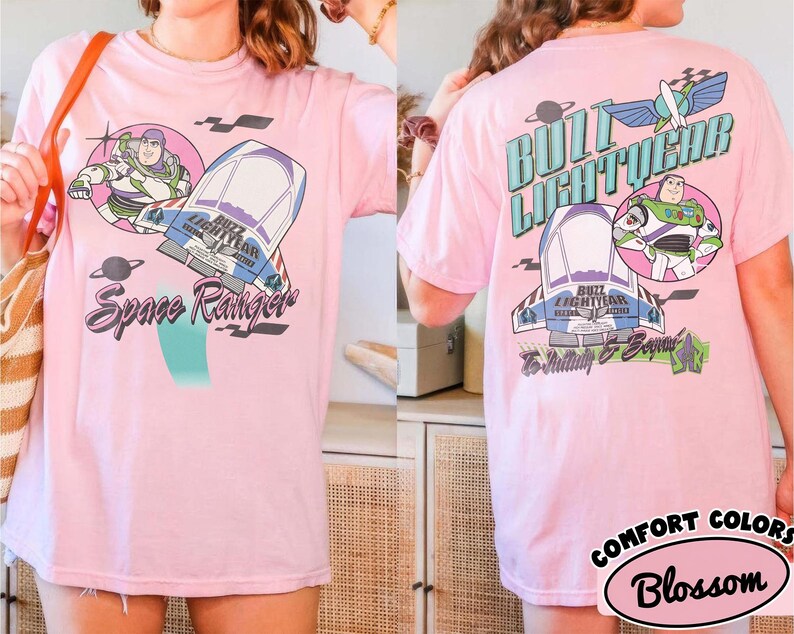 May include: A light pink t-shirt featuring Buzz Lightyear graphics on the front and back. The front displays Buzz Lightyear, a spaceship, and the text Space Ranger. The back shows Buzz Lightyear, a spaceship, and the text Buzz Lightyear To Infinity & Beyond.