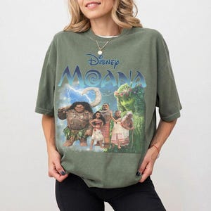 Pu&ograve; includere: T-shirt verde oliva con il film Disney "Moana". La grafica include il titolo del film e diversi personaggi, tra cui Maui, Moana e Te Fiti. La maglietta ha maniche corte e una vestibilit&agrave; ampia.