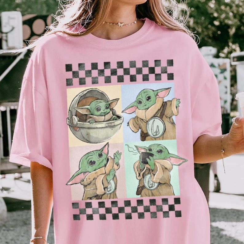 Puede incluir: Camiseta rosa claro con un dise&ntilde;o de cuatro paneles de un personaje alien&iacute;gena verde. El dise&ntilde;o est&aacute; enmarcado por patrones de cuadros blancos y negros. El personaje se muestra en una c&aacute;psula, sosteniendo una taza y gesticulando.