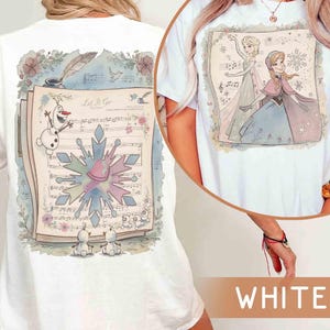 Pode incluir: Camiseta branca com uma ilustra&ccedil;&atilde;o do filme Frozen. A frente da camiseta mostra Elsa e Anna, enquanto a parte de tr&aacute;s mostra Olaf, um floco de neve e notas musicais. O texto "Let It Go" &eacute; vis&iacute;vel.