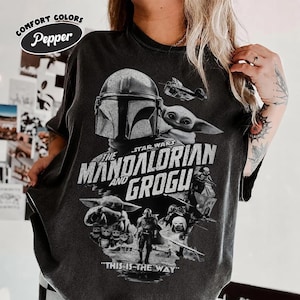 Peut inclure: T-shirt gris fonc&eacute; avec un graphisme de Star Wars repr&eacute;sentant Le Mandalorien et Grogu. Le design comprend le casque du Mandalorien, Grogu, et le texte "THE MANDALORIAN AND GROGU" et "THIS IS THE WAY". Le t-shirt porte les logos Comfort Colors et Pepper.