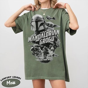 Peut inclure: Un t-shirt vert mousse avec un graphisme de la s&eacute;rie Star Wars, "The Mandalorian and Grogu". Le design comprend des images du Mandalorien, Grogu et le texte "THIS IS THE WAY". Le t-shirt est &eacute;tiquet&eacute; "Comfort Colors" et "Moss".