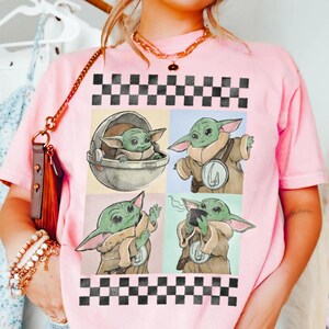Puede incluir: Camiseta rosa claro con un dise&ntilde;o de cuatro paneles de un personaje alien&iacute;gena verde en varias poses. El dise&ntilde;o incluye un borde a cuadros blanco y negro. El personaje se muestra en una c&aacute;psula, con una capa y una taza.