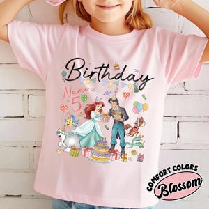 Pode incluir: Camiseta rosa claro com um gr&aacute;fico colorido de uma cena de anivers&aacute;rio. O design inclui a palavra "Birthday" em escrita preta, personagens de desenhos animados, bal&otilde;es e um bolo. O n&uacute;mero "5" tamb&eacute;m &eacute; vis&iacute;vel.