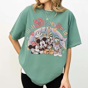 May include: Green t-shirt featuring a colorful graphic of Disney characters including Mickey and Minnie Mouse, Goofy, Donald Duck, and Pluto. The text "Walt Disney World" is arched above the characters, with a rainbow and castle in the background.