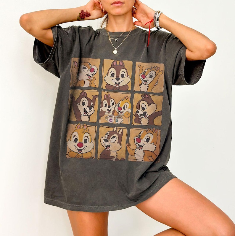 May include: Dark gray t-shirt featuring a grid of Chip and Dale cartoon character images. The graphic design includes various poses of the chipmunks in individual squares. The shirt has short sleeves and a relaxed fit.