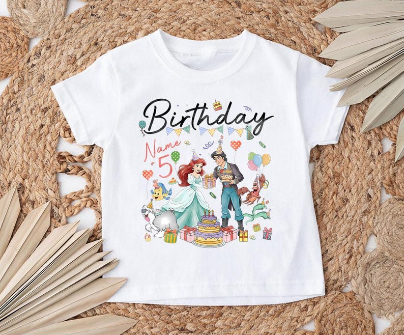 Pode incluir: T-shirt branco de manga curta com um gr&aacute;fico colorido de anivers&aacute;rio. O texto "Birthday" est&aacute; em preto, o n&uacute;mero "5" em rosa, com personagens de desenhos animados, um bolo e bal&otilde;es.